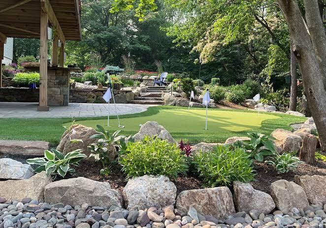 Residential putting green with landscaped garden beds, river rock, and boulders
